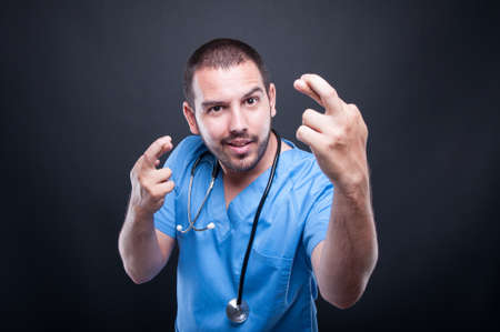 Portrait of male doctor with stethoscope showing double fingers croosed on black backgroundの写真素材