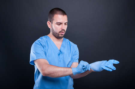 Doctor with scrubs putting on his latex gloves on black background with copy test spaceの写真素材