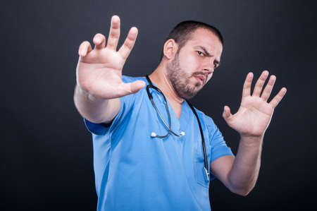 Doctor wearing scrubs with stethoscope making stay away gesture on black backgroundの写真素材