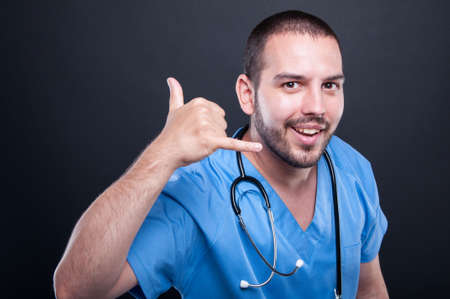 Doctor wearing scrubs with stethoscope making calling gesture smiling on black background