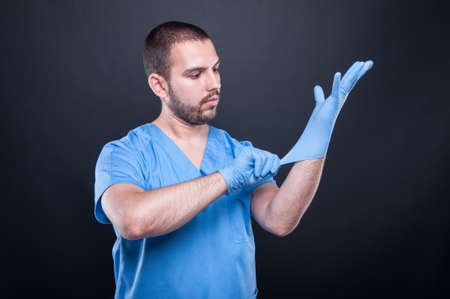 Doctor with scrubs putting on his latex gloves on black background with copy test spaceの写真素材
