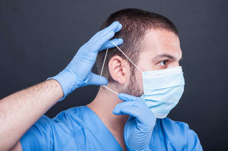 Side view doctor with scrubs and gloves putting on his sterile mask on black backgroundの写真素材