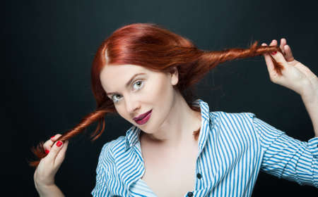 Young fashionable woman or model playing with her hair posing on dark backgroundの写真素材