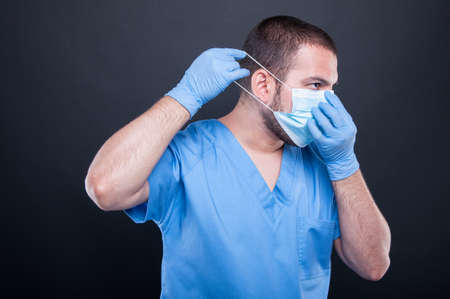 Side view doctor with scrubs and gloves putting on his sterile mask on black backgroundの写真素材