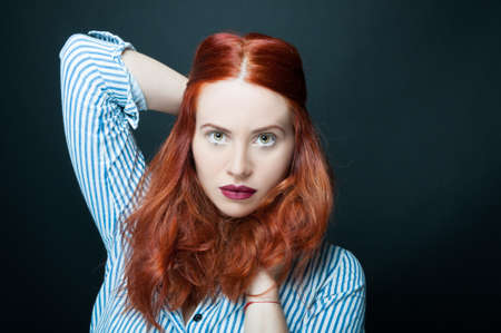 Beautiful and confident woman with long red hair posing in studio as fashion and beauty concept