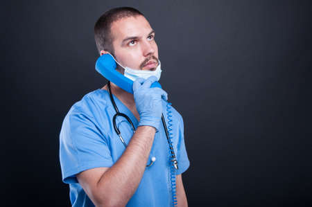 Doctor wearing scrubs holding telephone receiver on black background with copy text spaceの写真素材