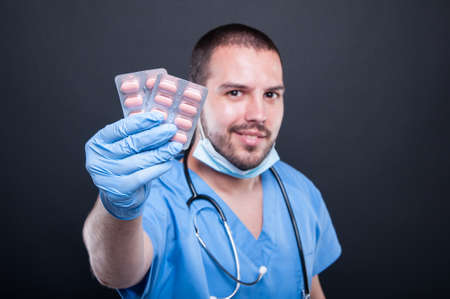 Selective focus of doctor wearing scrubs showing tablets blister and smiling on black backgroundの写真素材
