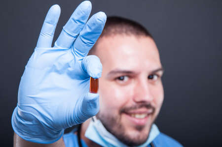 Selective focus of doctor wearing scrubs holding one pill and smiling on black background