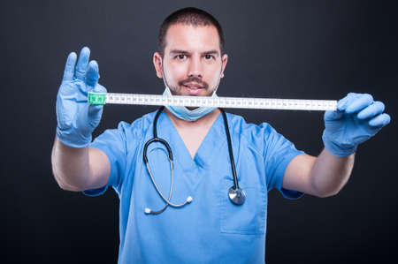 Plastic surgeon wearing scrubs showing measuring tape and smiling on black backgroundの写真素材