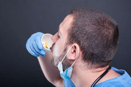 Side view of doctor wearing scrubs sipping from cup with pills on black backgroundの写真素材