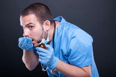Doctor wearing scrubs taking pills from bottle like hiding from someone on black backgroundの写真素材