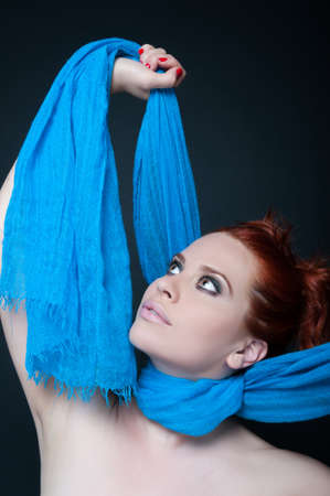 Modern stylish female with red hair rising up her scarf on dark backgroundの写真素材
