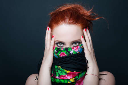 Young redhead girl with floral scarf over mouth posing on dark backgroundの写真素材