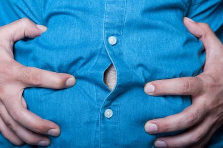 Man hold hands over his swollen abdomen in closeup view as cramp and bloating conceptの写真素材
