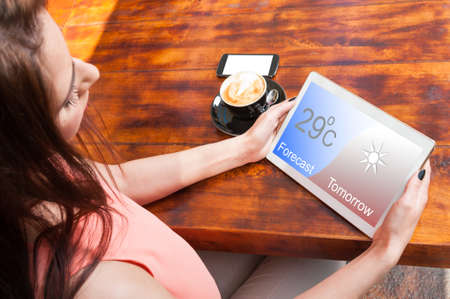 Beautiful woman watching forecast on her tablet and drinking a fresh coffeeの写真素材