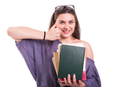 Cheerful student doing like sign and holding books in her hands isolated on white backgroundの写真素材