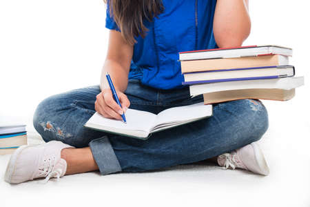 Close-up of student girl sitting writing in notebook with books around isolated on white background