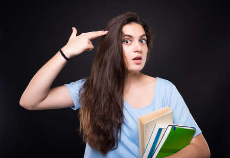Student female looking bored of study shooting herself with finger gun gestureの写真素材