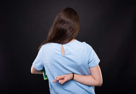 Girl model with books standing with fingers crossed in back view as bad luck concept