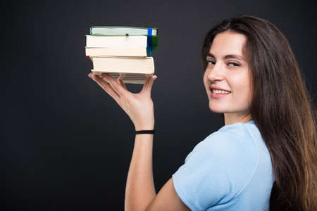 Smiling student girl holding up some books and smiling cheerfullyの写真素材