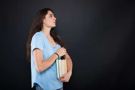 Serious female student with books looking one side on dark background with copy spaceの写真素材