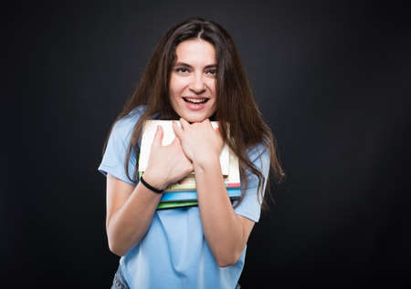 Pretty young college girl smiling and hugging her books on dark backgroundの写真素材