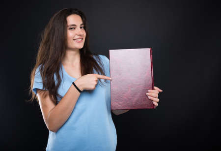 Cheerful girl student pointing at her album after finising schoolの写真素材