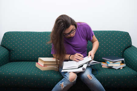 Pretty teenage woman writing notes from books preparing for examsの写真素材