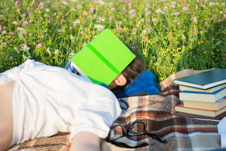 Woman sleeping on the grass outside while reading a bookの写真素材