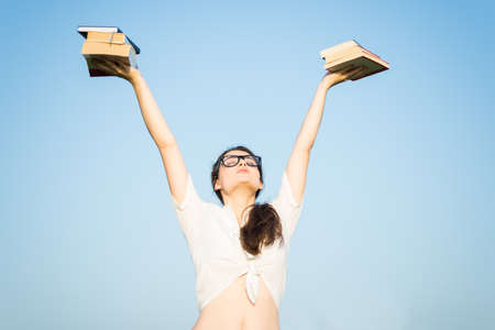 Free girl rising arms with books in the air in a sunny summer day feeling happy and relaxedの写真素材