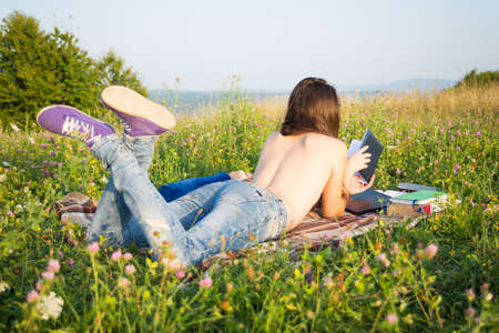 Young naked woman reading book on summer field relaxing in her freetimeの写真素材