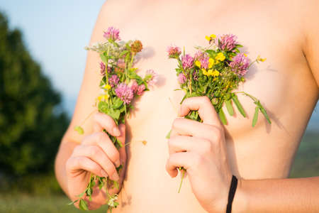 Closeup view of topless woman holding flowers and covering her chestの写真素材