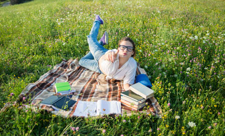 Young caucasian woman reading a book outdoor on green grass and pointing at youの写真素材