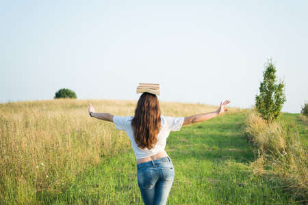 Free girl with school books above head to create balance walking outside