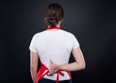 Rear view of girl seller rising thumb up behind her back isolated on dark backgroundの写真素材