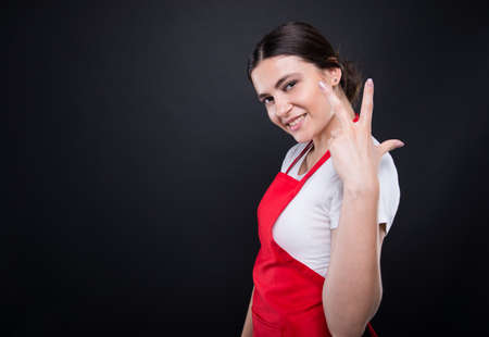 Cheerful seller rising three fingers and smiling on dark background with copyspaceの写真素材