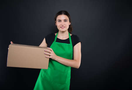 Beauiful girl clerk holding a big box in her arms for the store on dark background