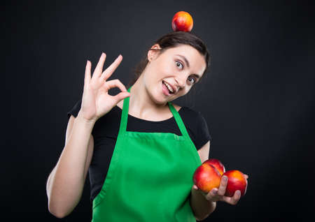 Cheerful young seller holding many nectarines and promoting a healthy lifestyleの写真素材