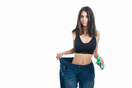 Fit girl wearing big size pants holding measuring tape like loosing weight concept isolated on white backgroundの写真素材