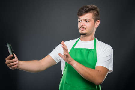 Portrait supermarket employer looking strange at smartphone on black background