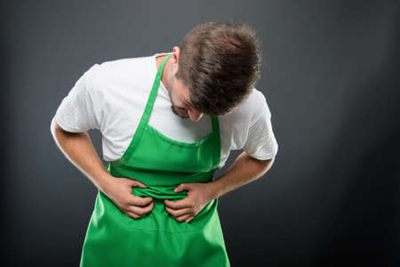 Portrait of supermarket employer holding belly like hurting on black background