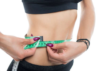 Close-up of fit girl abs measuring with tape isolated on white background