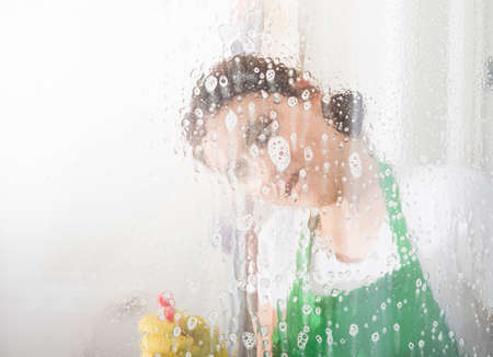 Housekeeping woman cleaning window with spray to remove dust and stains