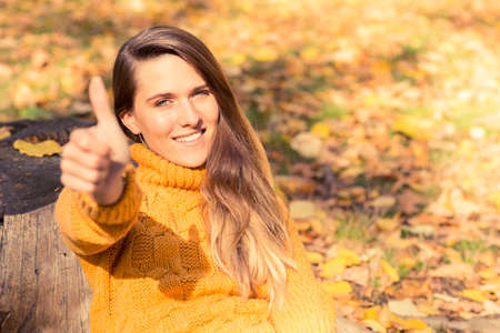 Smiling woman relaxing in colorful forest foliage outdoor and rising thumb upの写真素材