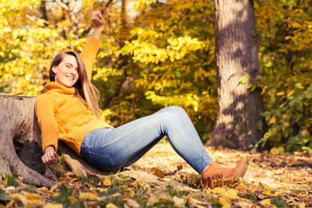 Happy young woman with autumn yellow leaves enjoying the good weather outside