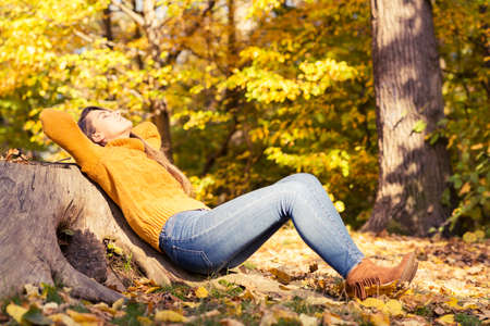 Beautiful woman standing in a forest in autumn enjoying the bright warm sunの写真素材