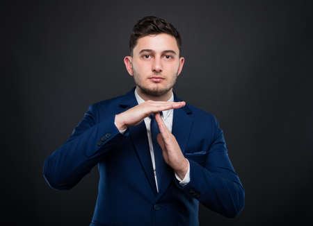 Handsome entrepreneur showing time out sign or interrupting something on black backgroundの写真素材