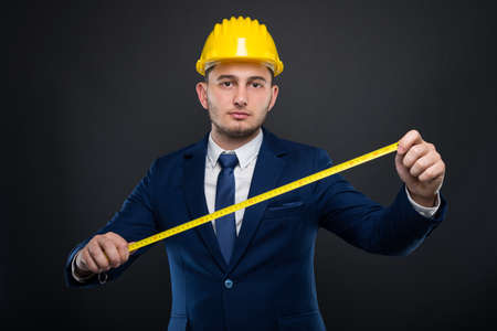 Male builder with helmet holding a meter or tape measure at his job on dark backgroundの写真素材