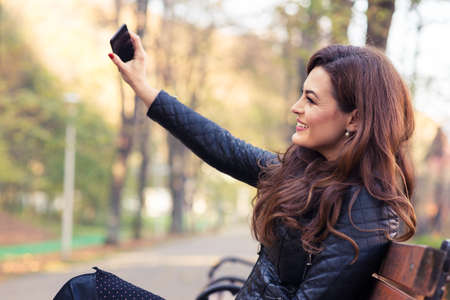 Stylish modern girl taking a selfie with smart phone in autumn park