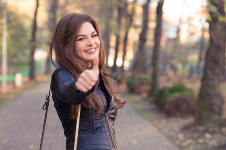 Gorgeous girl in autumn park rising thumb up looking happy and smilingの写真素材